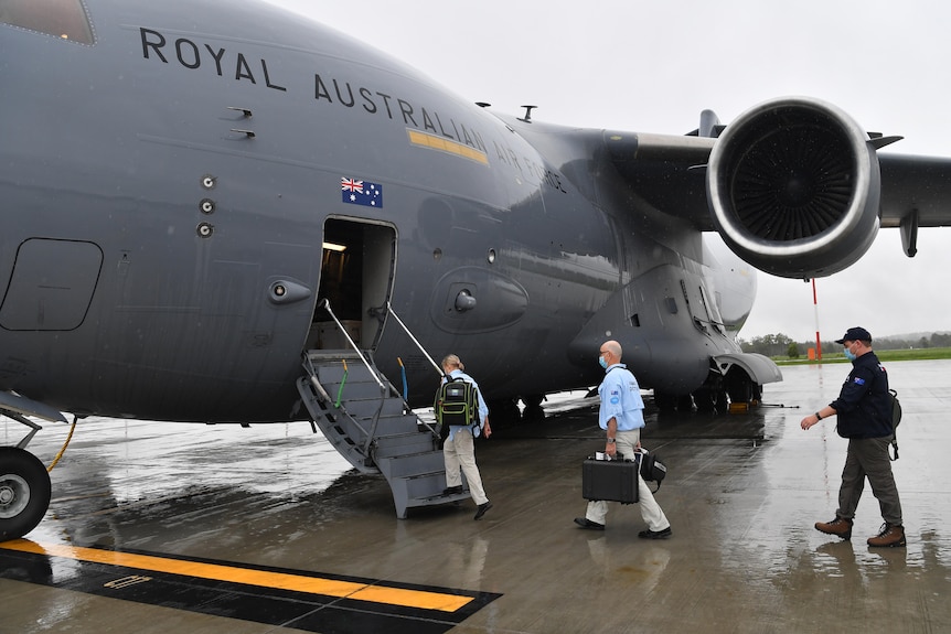 Two people in blue shirts board a large RAAF aircraft.