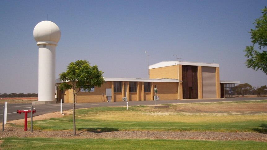 Brick building with a tall (maybe 3 storey) white pole with large globe on top next to it.