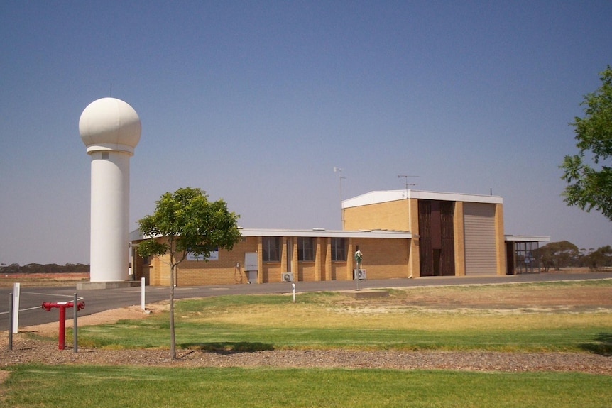 Brick building with a tall (maybe 3 storey) white pole with large globe on top next to it.