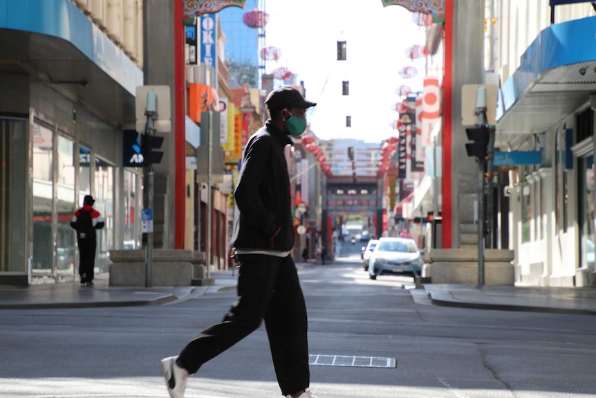 Un hombre camina con una máscara en Melbourne a principios de septiembre de 2020, con Chinatown de fondo.