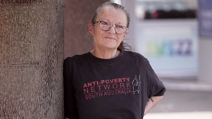A woman wearing an anti-poverty shirt leans against a wall.