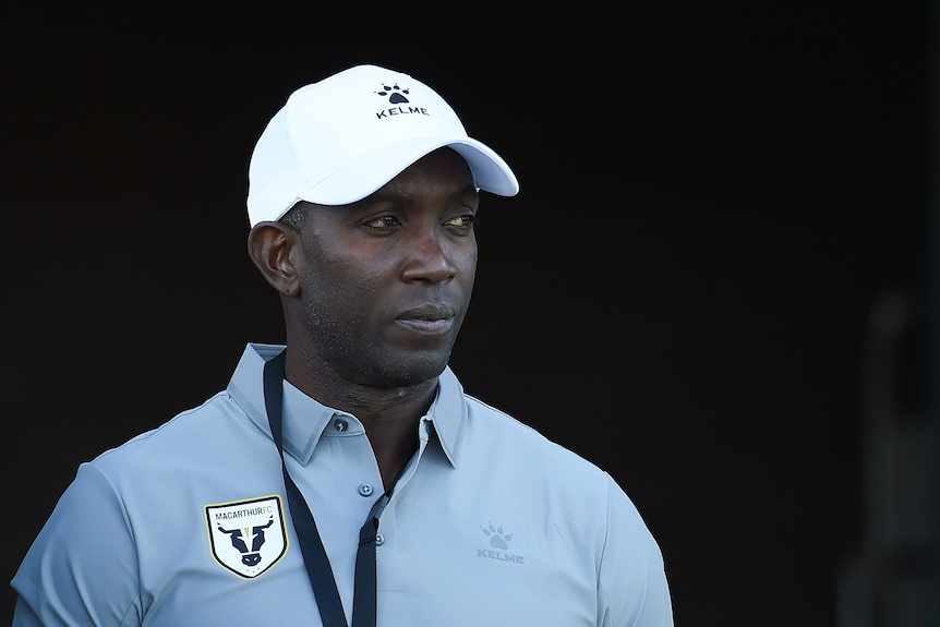 Dwight Yorke stands wearing a cap with a neutral expression on his face