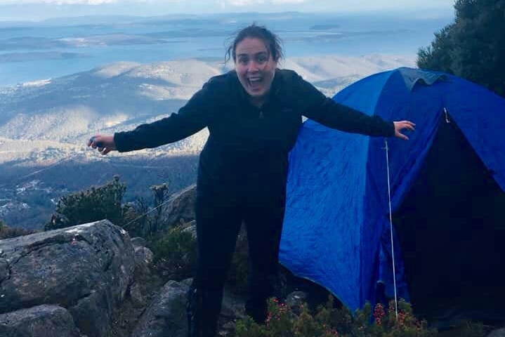 A woman on a mountain with a blue tent behind her