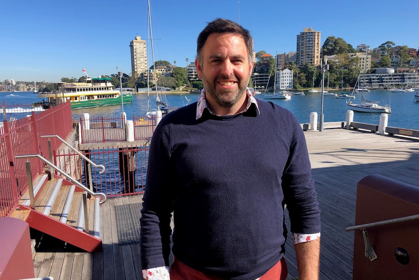 A man stands on the pier at Luna Park and looks at the camera, he is smiling