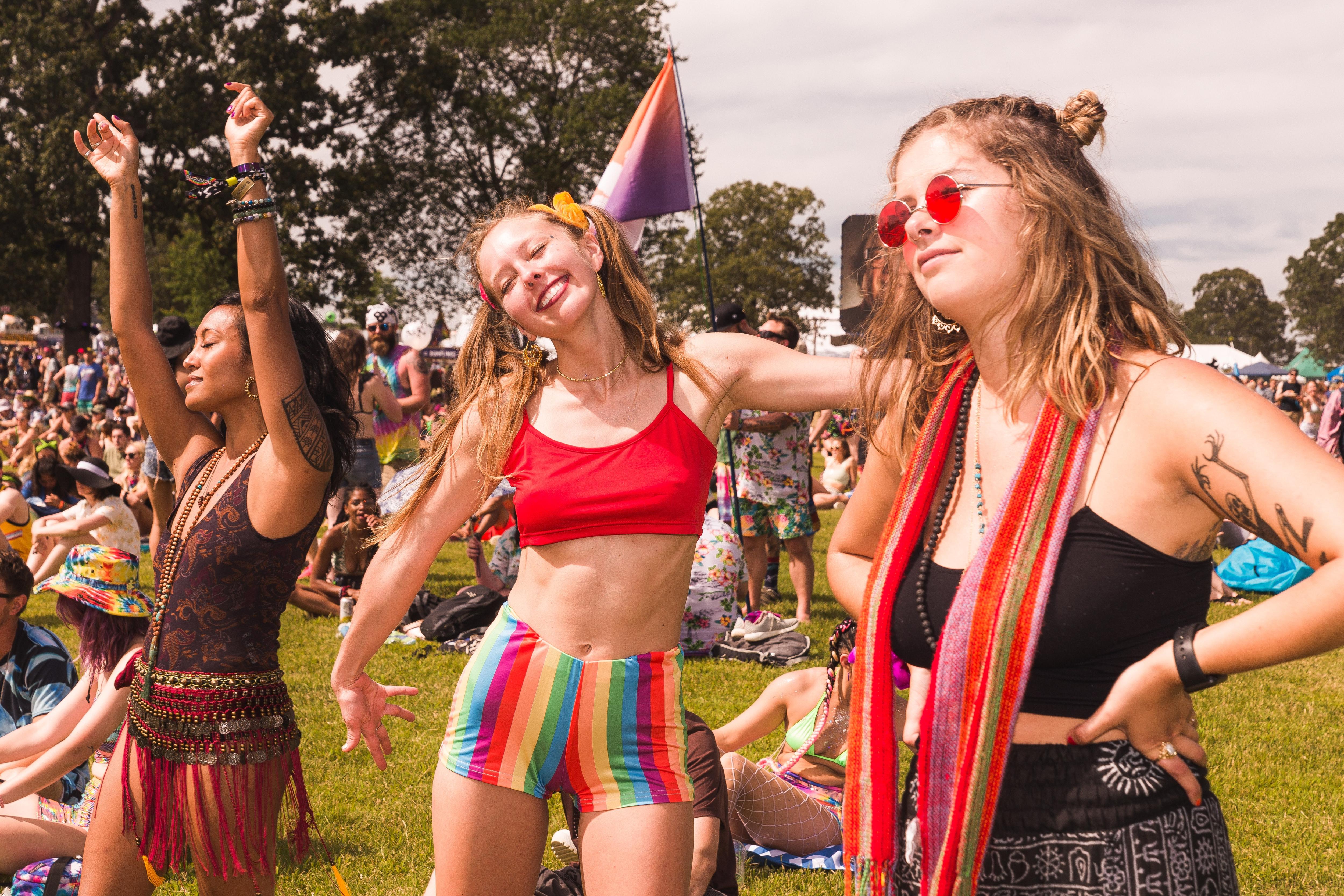 A woman wearing rainbow shorts and pig tails poses at a festival, next to another woman dancing and another looking on.