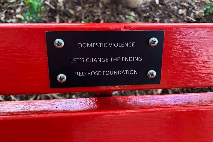 A plaque on a red bench.