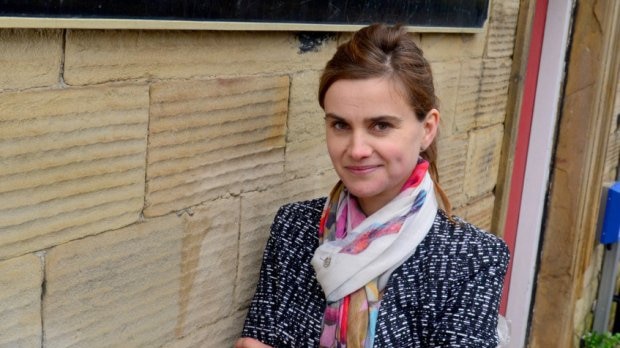 British Labour MP Jo Cox leans against a wall wearing a scarf and a jacket.