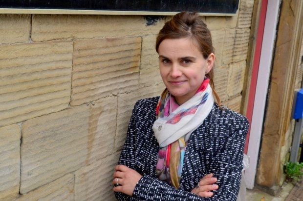 British Labour MP Jo Cox leans against a wall wearing a scarf and a jacket.