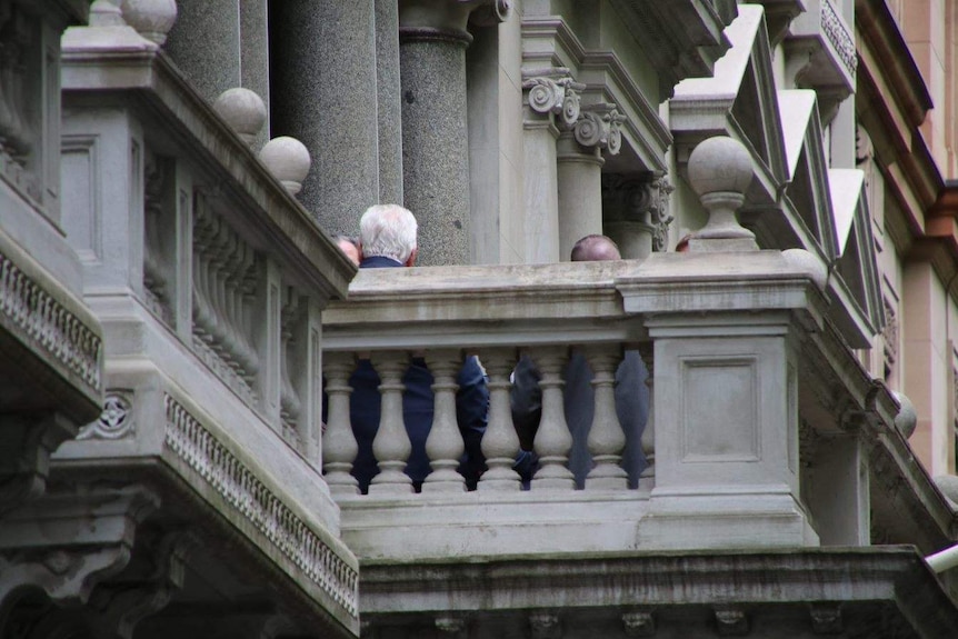 An elaborate balcony where the tops of unidentifiable men's heads can be seen.