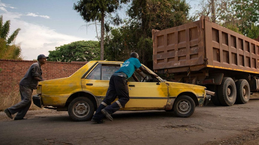 two men push a car along the road