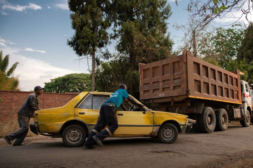 two men push a car along the road