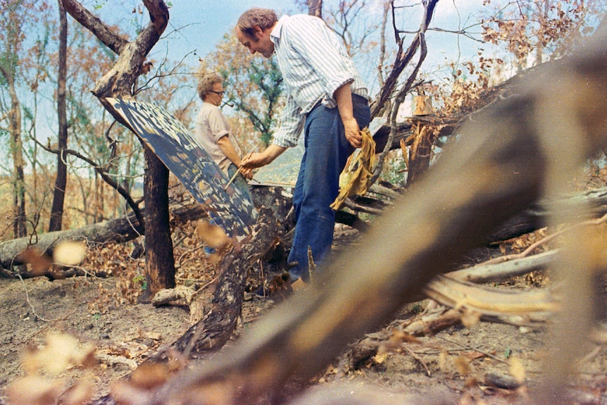 Two men paint on canvases standing in the bush