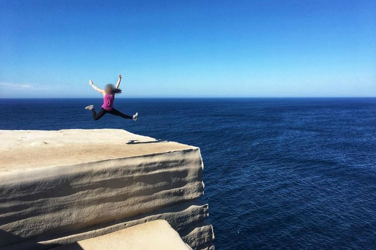 A woman jumps on a cliff top
