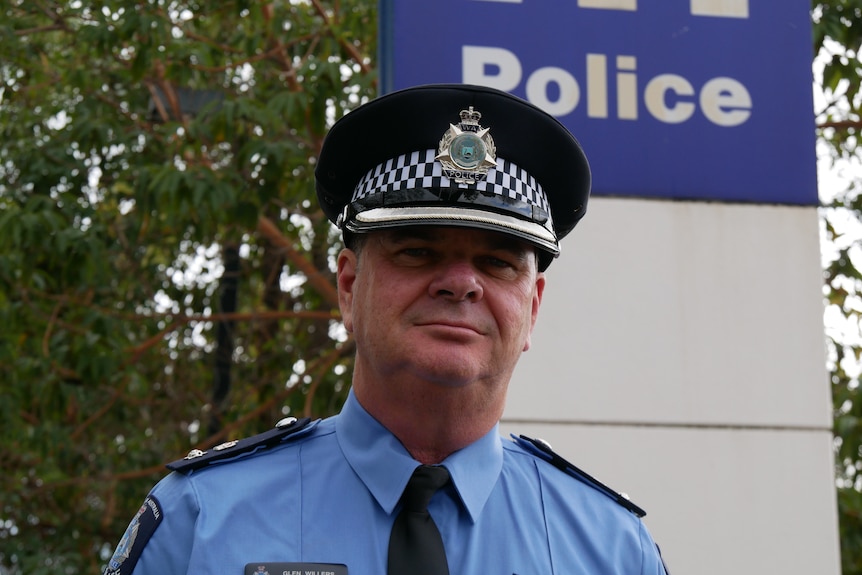 A police officer stands in front of a sign saying police.