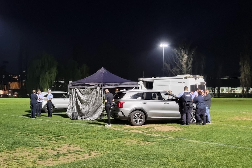 A pop-up tent, cars and police officers on a sports oval. 