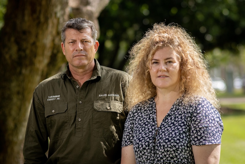 A man and a woman standing next to each other, not smiling.