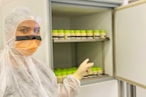 A worker in PPE points to a storage refrigerator of powdered breast milk.