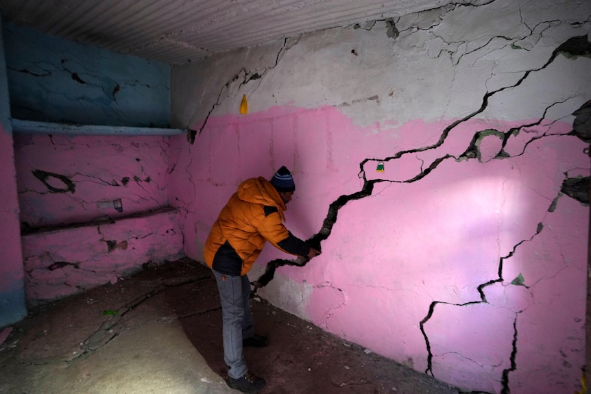 A man places his hand in a large crack in a pink wall. 