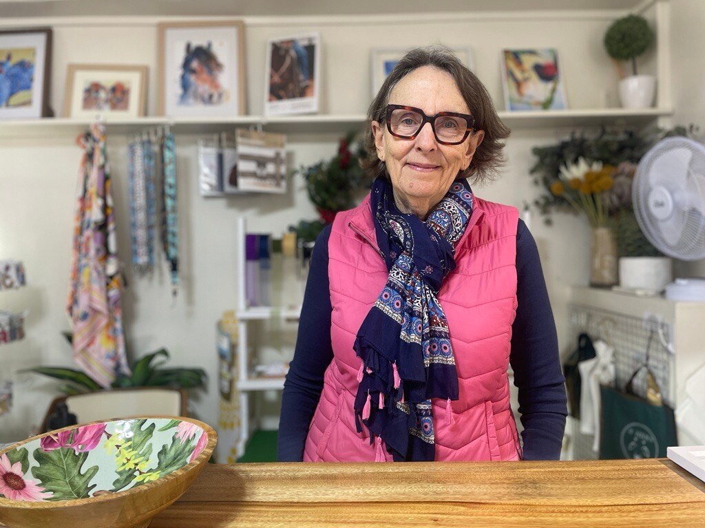 Older woman wearing a scarf and pink vest looking at camera. 