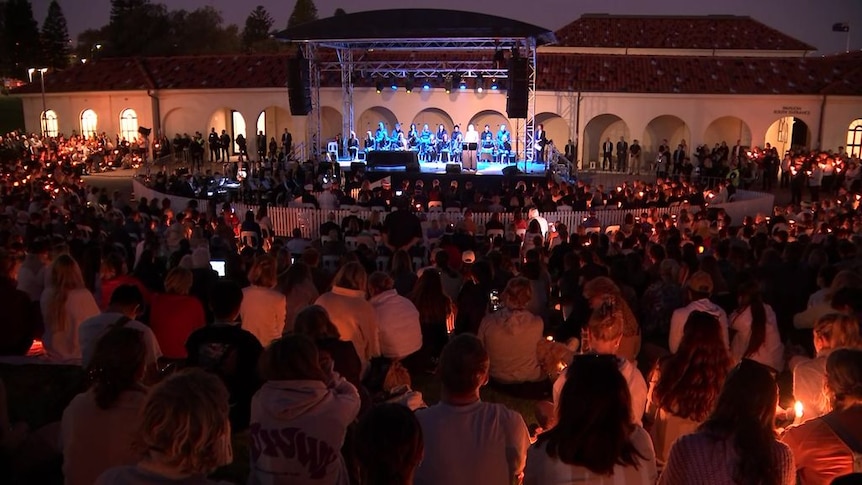 A crowd of people holding candles gather around a stage.