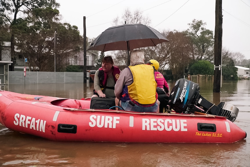 three elderly people, one holding an umbrella being rescued in a boat during a flooding event