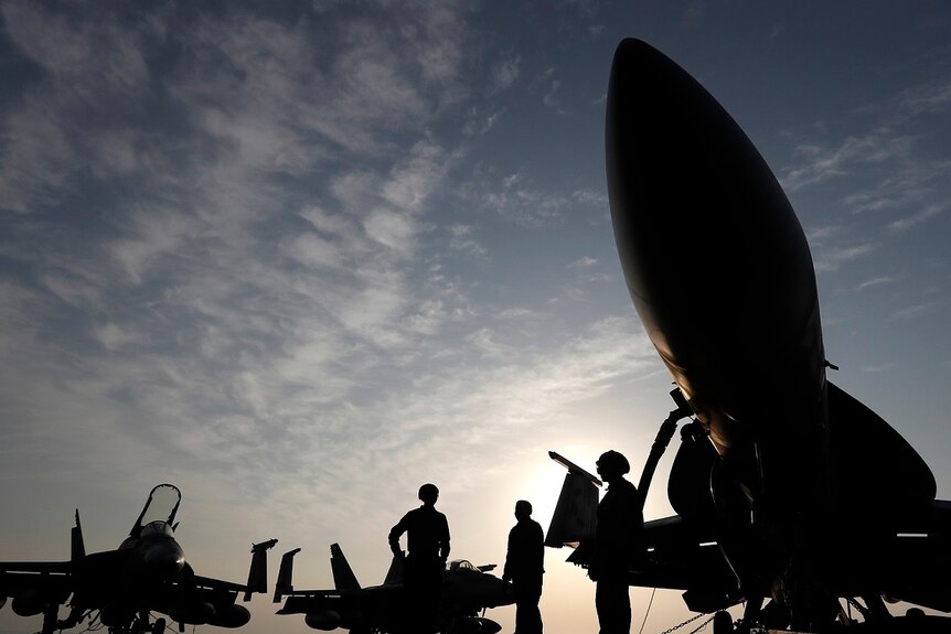 US Navy soldiers and aircraft silhouetted against the sky