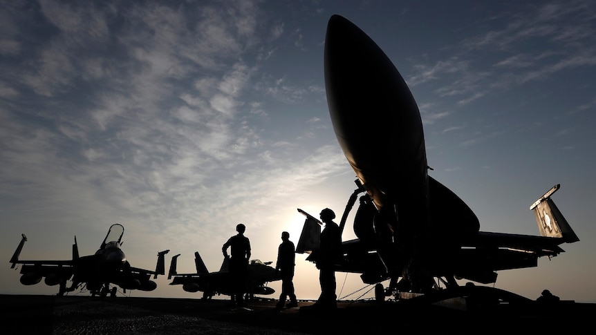 US Navy soldiers and aircraft silhouetted against the sky