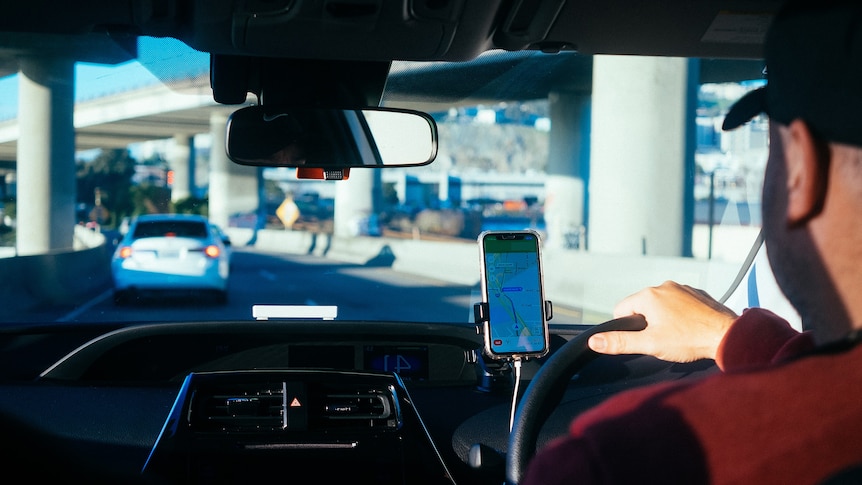 A rideshare driver behind the wheel with a map of streets on his phone.