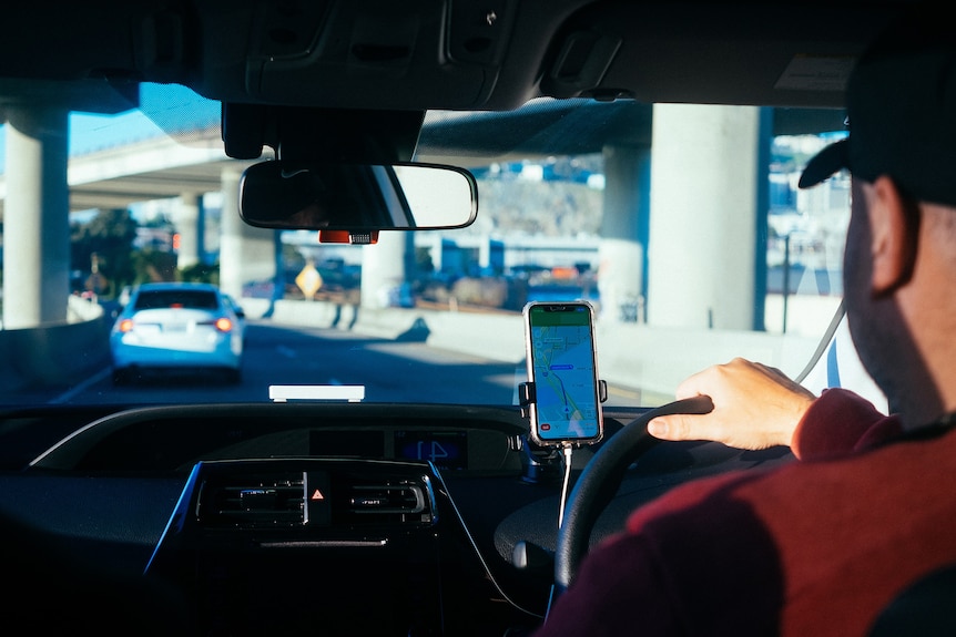 A rideshare driver behind the wheel with a map of streets on his phone.