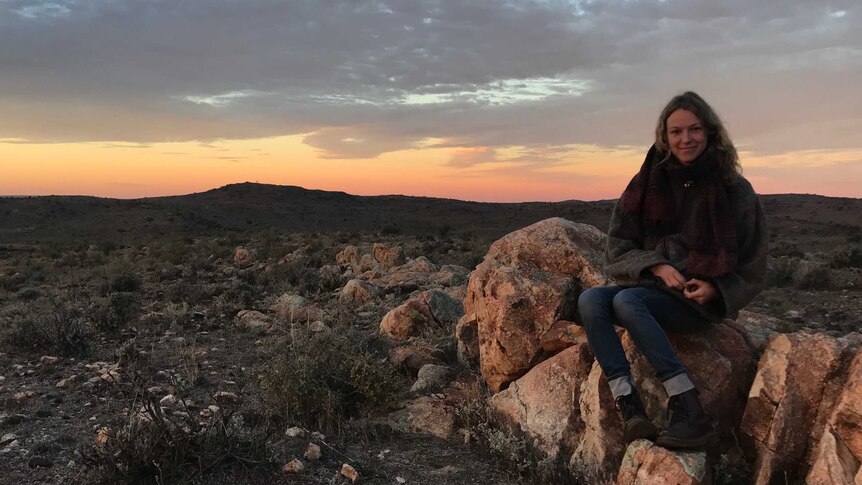 A woman sits on a rocky outcrop in scrubby outback