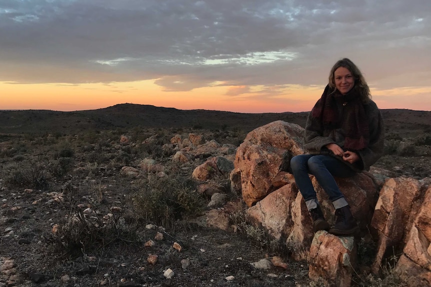 A woman sits on a rocky outcrop in scrubby outback
