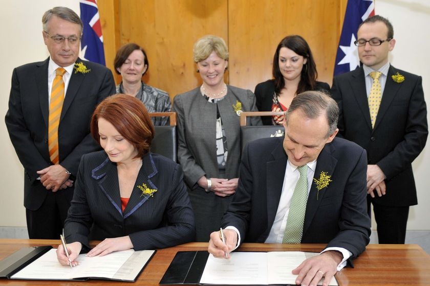Julia Gillard and Bob Brown sign on the line (AAP: Alan Porritt)