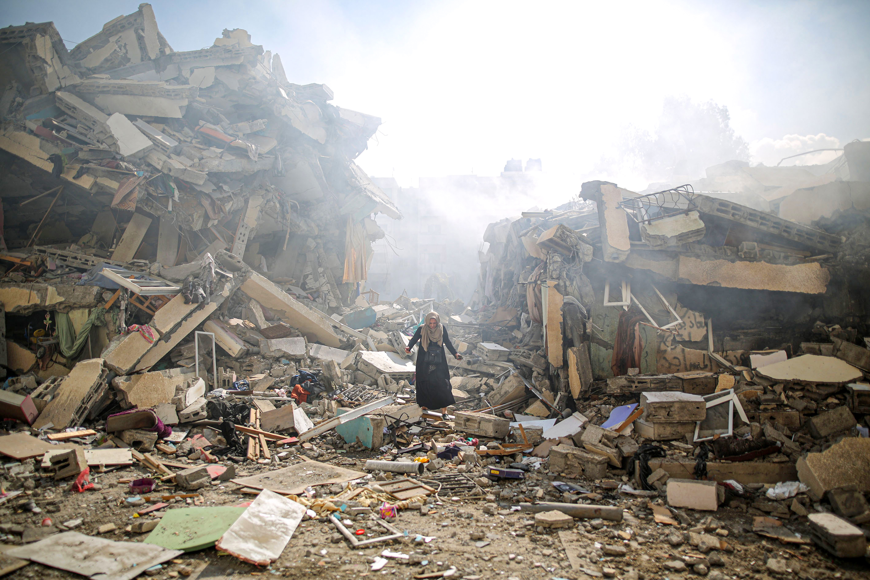 A person stands in the rubble of destroyed buildings, with rubble all over the street