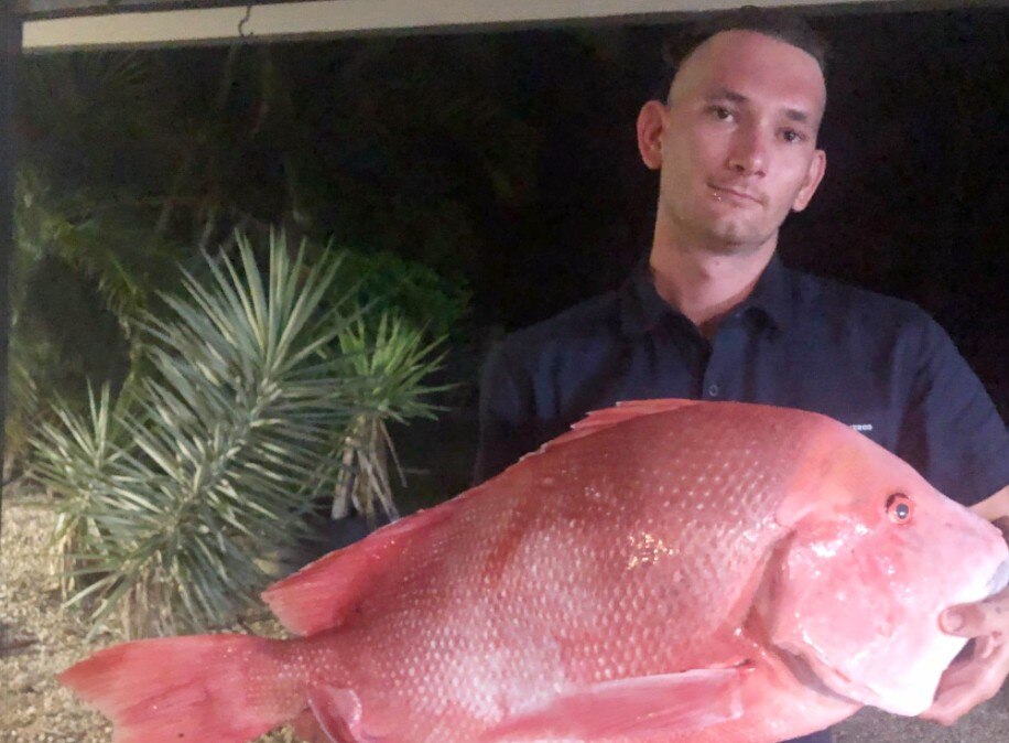 A young man looking at the camera, holding a big red fish