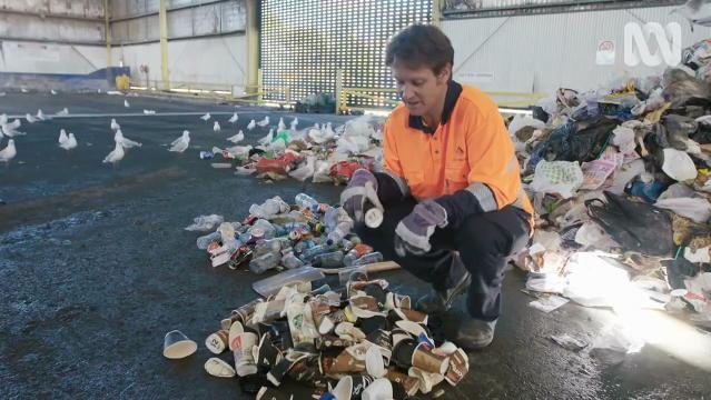 Craig Reucassel crouches beside pile of used paper takeaway coffee cups