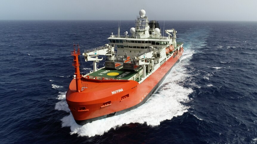 Large orange ship ploughing through dark blue ocean, with white spray washing up 