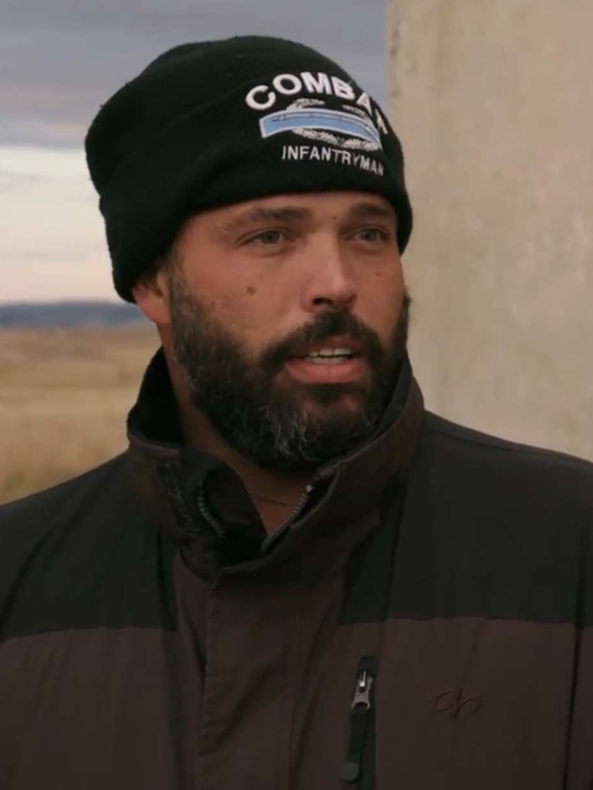 A man in a beanie stands outside a concrete bunker.