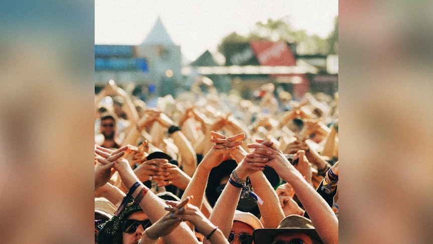 a large crowd of people at a music festival hold their hands aloft