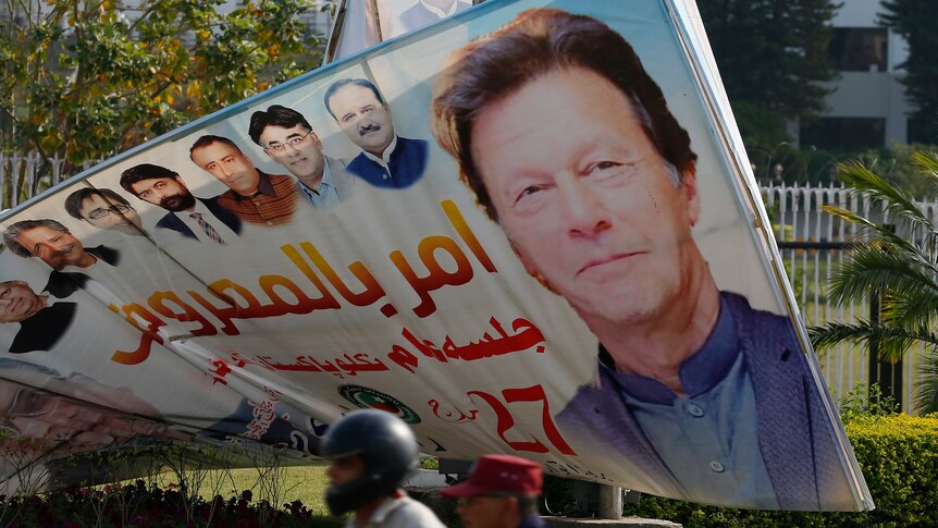 A motorcyclist passes a large sign with a picture of Imran Khan's face outside the National Assembly.