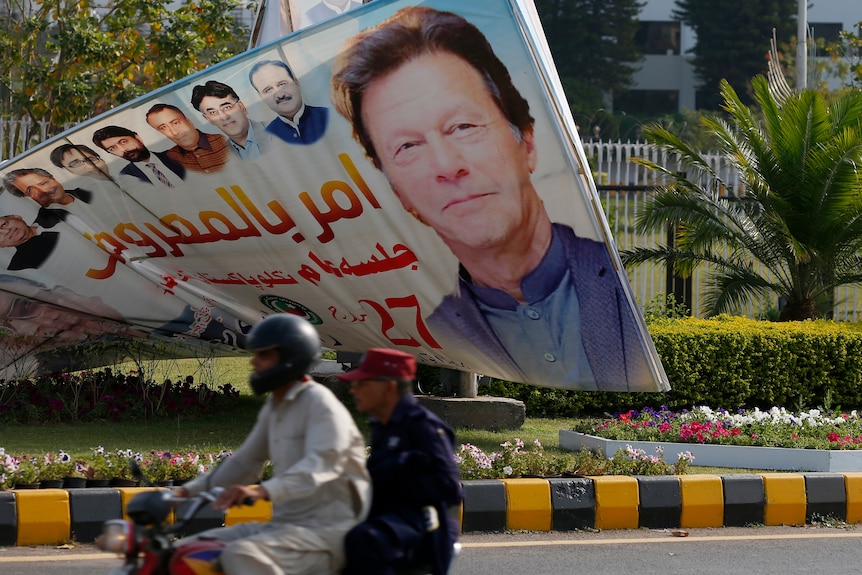 A motorcyclist passes a large sign with a picture of Imran Khan's face outside the National Assembly.