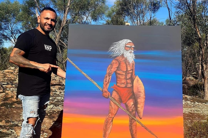 A man pointing to a very tall painting of an Aboriginal man.