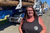Woman stands besides long semi-trailer logging truck