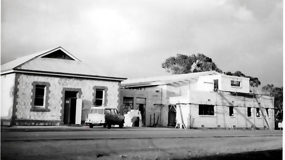 Black and white photograph of an old streetscape featuring a car and a construction site of a large building