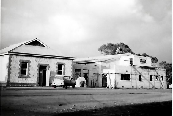 Black and white photograph of an old streetscape featuring a car and a construction site of a large building