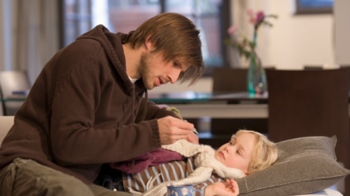 Man takes the temperature of unwell child lying down in bed.