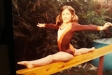 An old photo of a young girl in a leotard doing the splits on a balance beam.