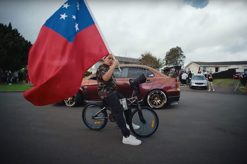 A young person on a bike with a siren attached to it waves a Samoan flag in the video for Savage Love