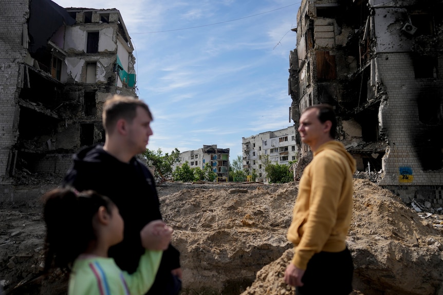 People stand in front of a building damaged by shelling