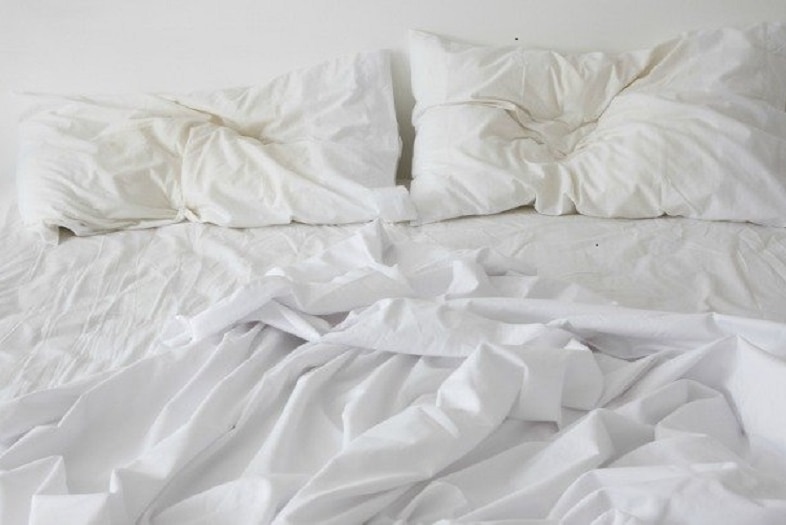 White bed sheets on a bed which have been used, are unmade and crinkled.