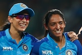 Smriti Mandhana puts her arm around Harmanpreet Kaur as they walk off smiling after India beat Australia in a T20 cricket match.